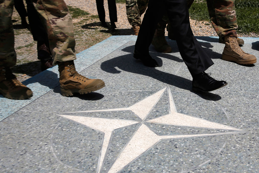 U.S. Defense Secretary James Mattis, in black dress shoes, walks with U.S. Army leaders across a NATO logo, April 2017. (AP/Jonathan Ernst)