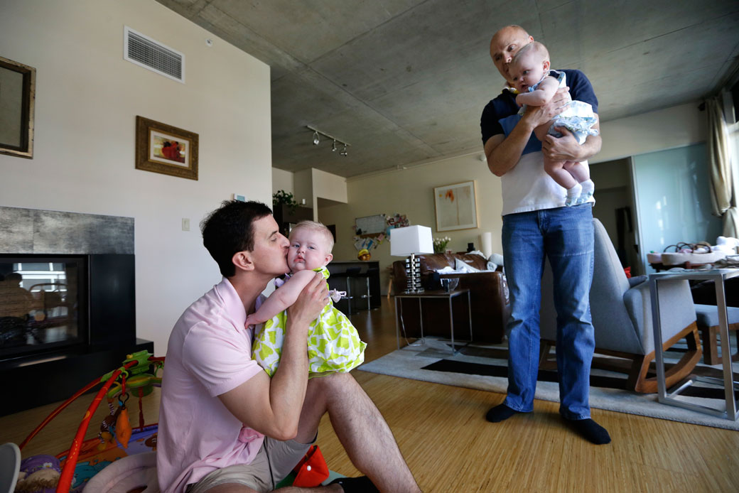Trey Powell, left, kisses his daughter, Ashton, as nanny Randy Hambley holds her twin sister, Kylan, in Powell's home in Seattle, August 20, 2013. (AP/Elaine Thompson)