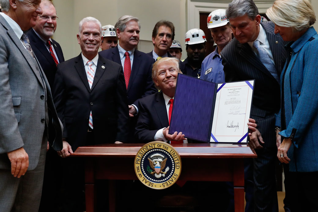 In this February 16, 2017, photo, Sen. Shelley Moore Capito (R-WV), right, Sen. Joe Manchin (D-WV), second from right, and coal miners watch as President Donald Trump holds up H.J. Res. 38 after signing it in the Roosevelt Room of the White House in Washington. (AP/Carolyn Kaster)