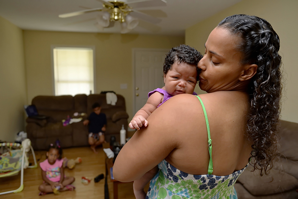 A Mother holds her 2-month-old baby as her children sit in their home in Greenville, South Carolina, June 2014. (AP/Richard Shiro)