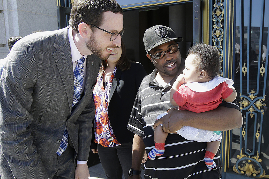 A father holds his 6-month-old son as he speaks with former San Francisco Supervisor Scott Wiener, left, before a rally supporting paid family leave at City Hall in San Francisco, April 5, 2016. (AP/Jeff Chiu)