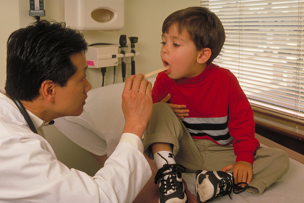 A doctor checks the throat of a young boy. (Getty/Education Images)