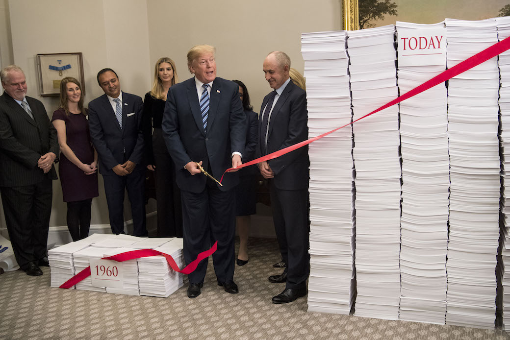 President Donald Trump cuts the ribbon across two stacks of paper symbolizing deregulation at a White House event, Washington, D.C., December 2017. (Getty/Carolyn Van Houten/The Washington Post)