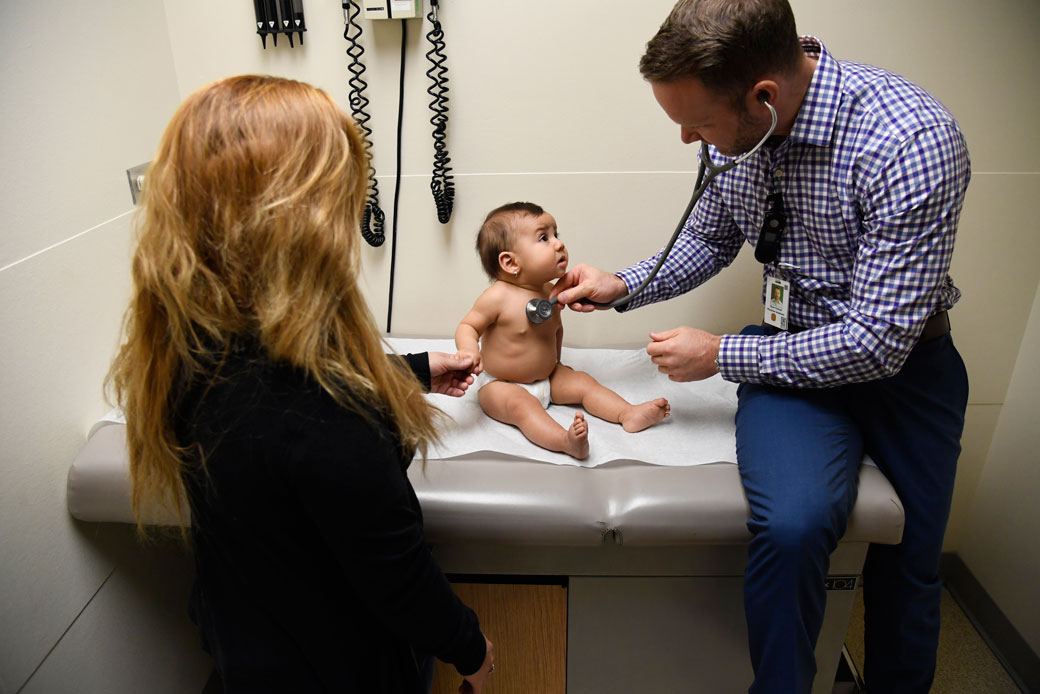 A physician assistant examines a patient as her mother holds her hand, January 2018. (Getty/The Denver Post/Andy Cross)