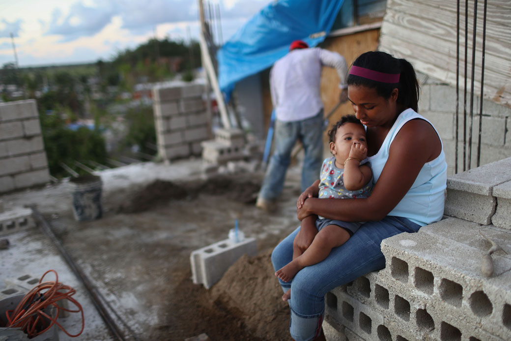 A mother holds her baby as her husband works to reconstruct their home destroyed by Hurricane Maria in San Isidro, Puerto Rico, on December 23, 2017. (Mario Tama/Getty)