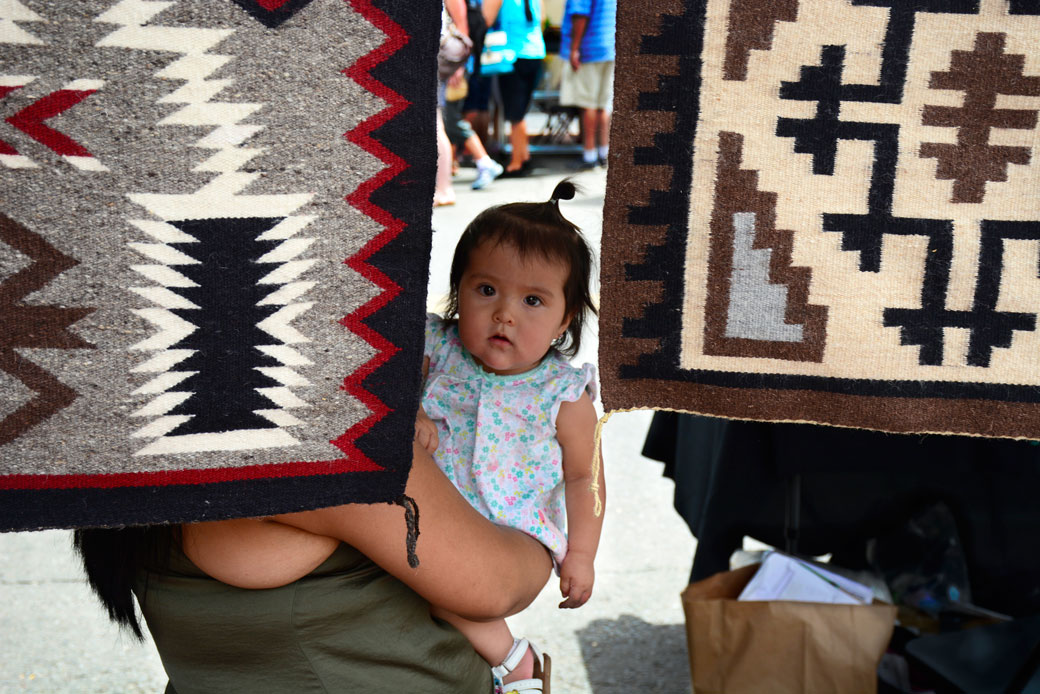 A Navajo mother and weaver holds her Native American daughter in her booth at the Santa Fe Indian Market in Santa Fe, New Mexico. (Getty/Robert Alexander)