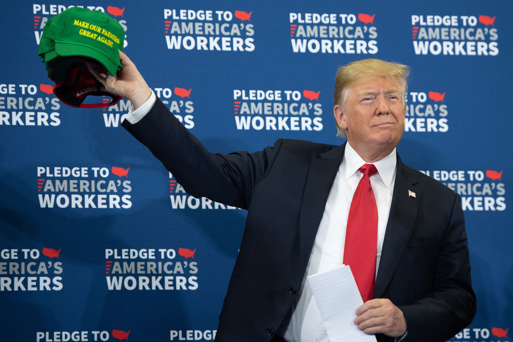 U.S. President Donald Trump holds up hats as he arrives for a roundtable discussion on workforce development in Peosta, Iowa, on July 26, 2018. (Getty/AFP/Saul Loeb)