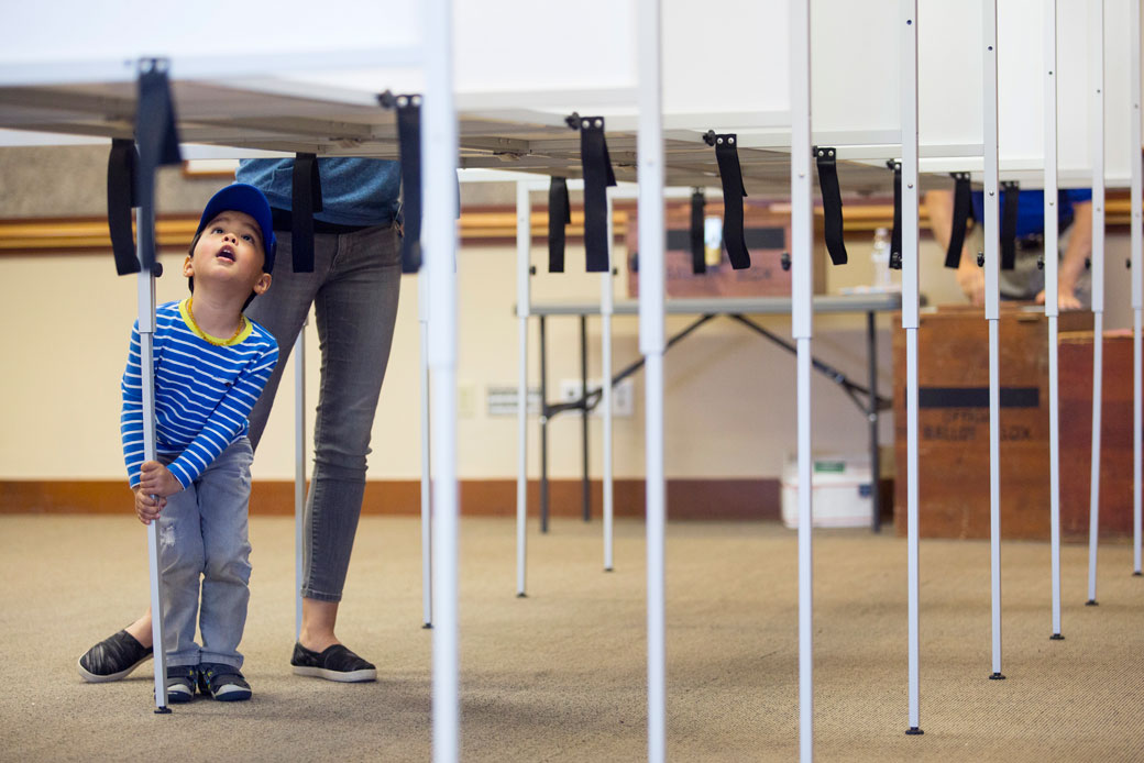 A child peers up into a voting booth as his mother fills out ballots in Scarborough, Maine. (Getty/Portland Press Herald/Derek Davis)