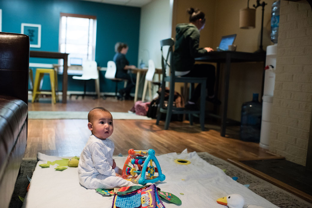 A 6-month-old child plays on a mat while his mother works nearby, Chantilly, Virginia, January 2017.