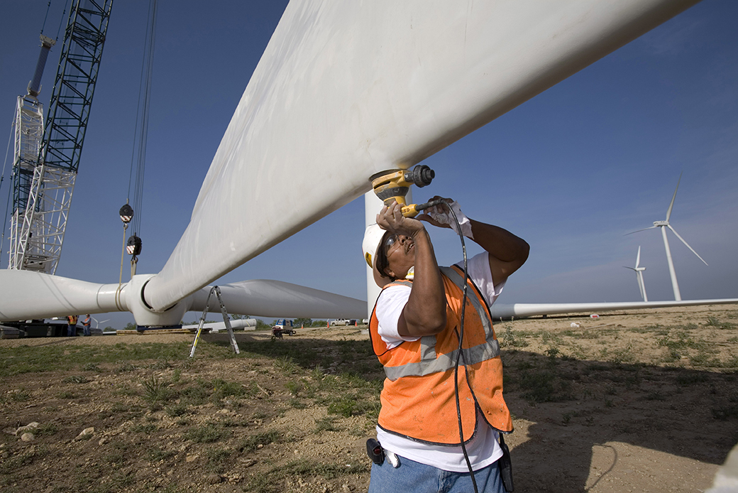 With the help of a crane, construction workers sand the surface of a propeller at a tower base on a Texas wind farm, June 2007. (Getty/Robert Nickelsberg)