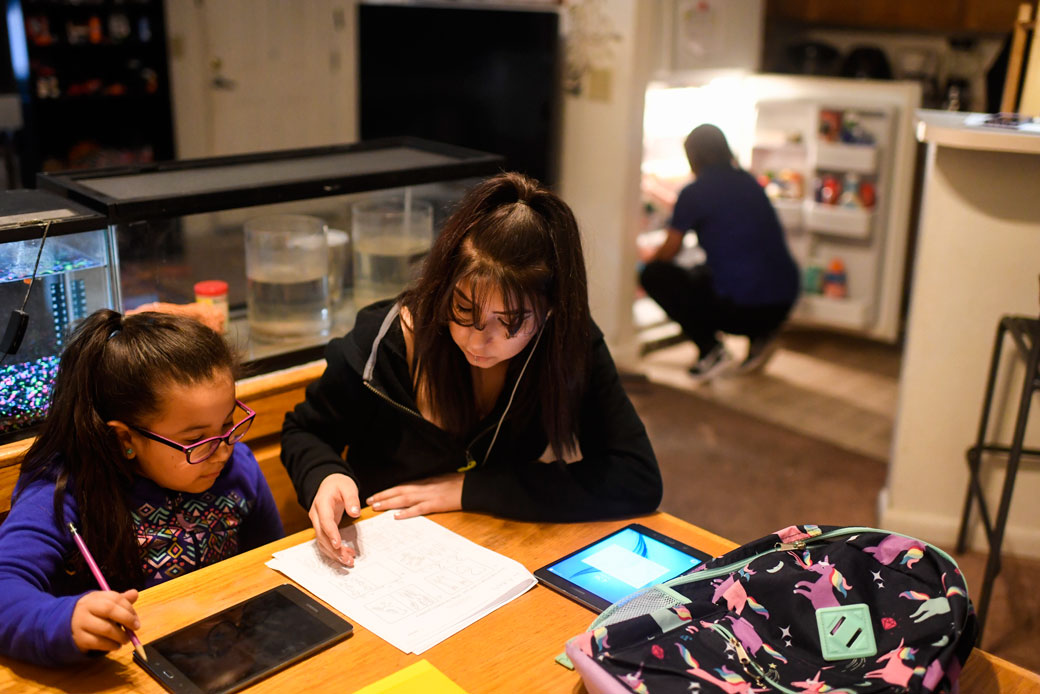 A teenager helps her younger sister complete her math homework at their Denver home, January 2018. (Getty/The Denver Post/AAron Ontiveroz)