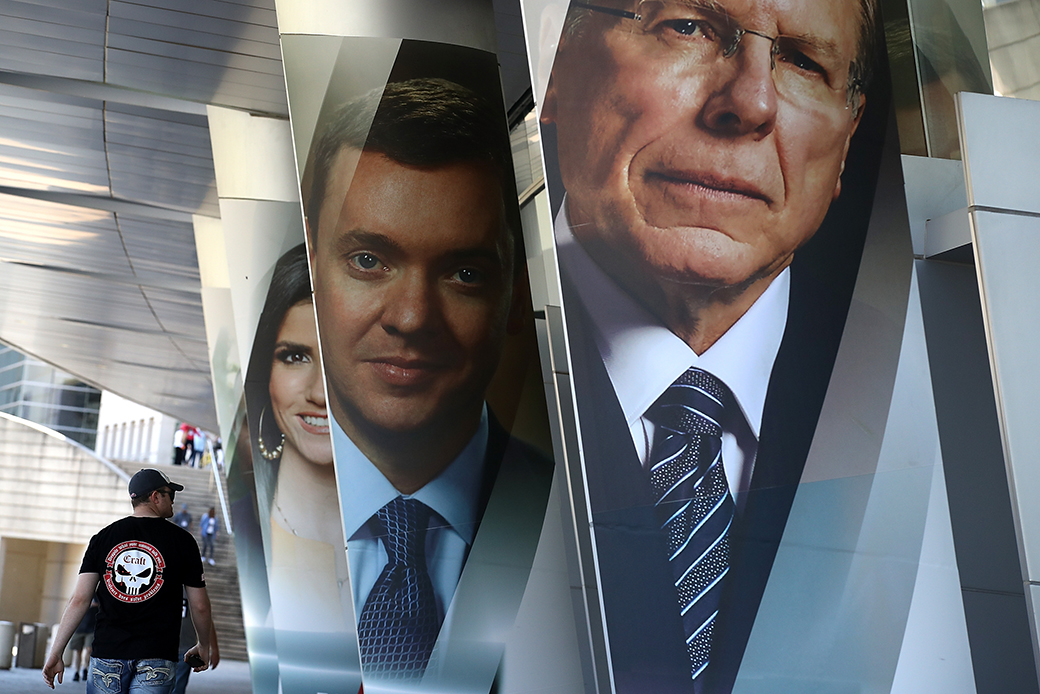 An attendee walks by photographs of National Rifle Association executive vice president and CEO Wayne LaPierre (R), NRA chief lobbyist Chris Cox, and NRATV commentator Dana Loesch outside the NRA Annual Meeting and Exhibits at the Kay Bailey Hutchison Convention Center on May 5, 2018, in Dallas. (Getty/Justin Sullivan)