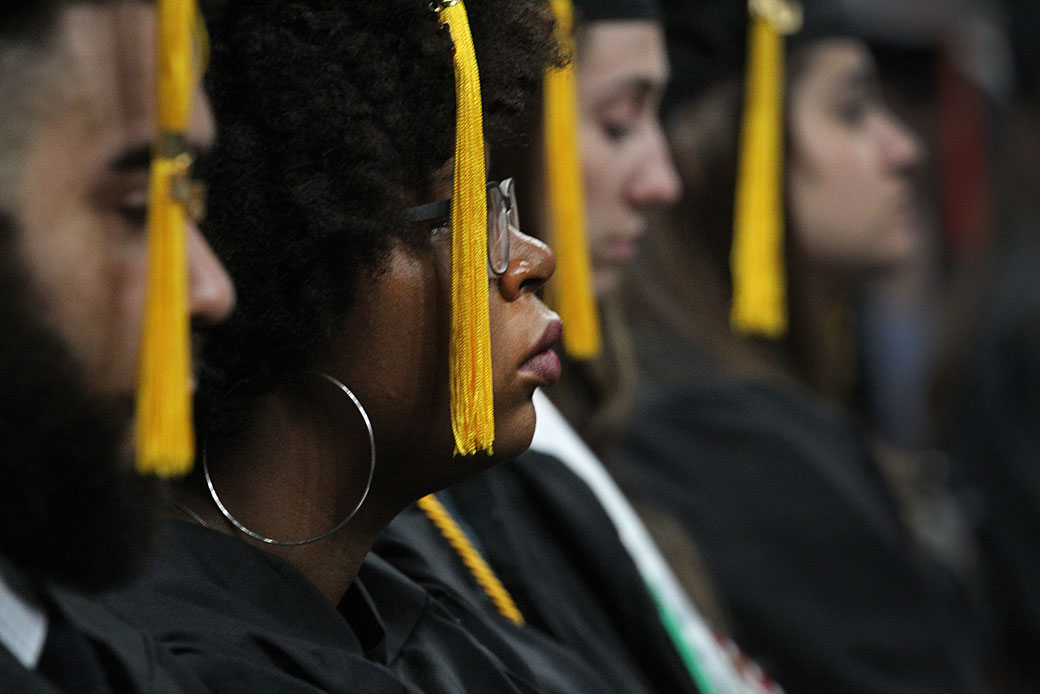  (A woman wearing a graduate cap listens at her college graduation ceremony.)
