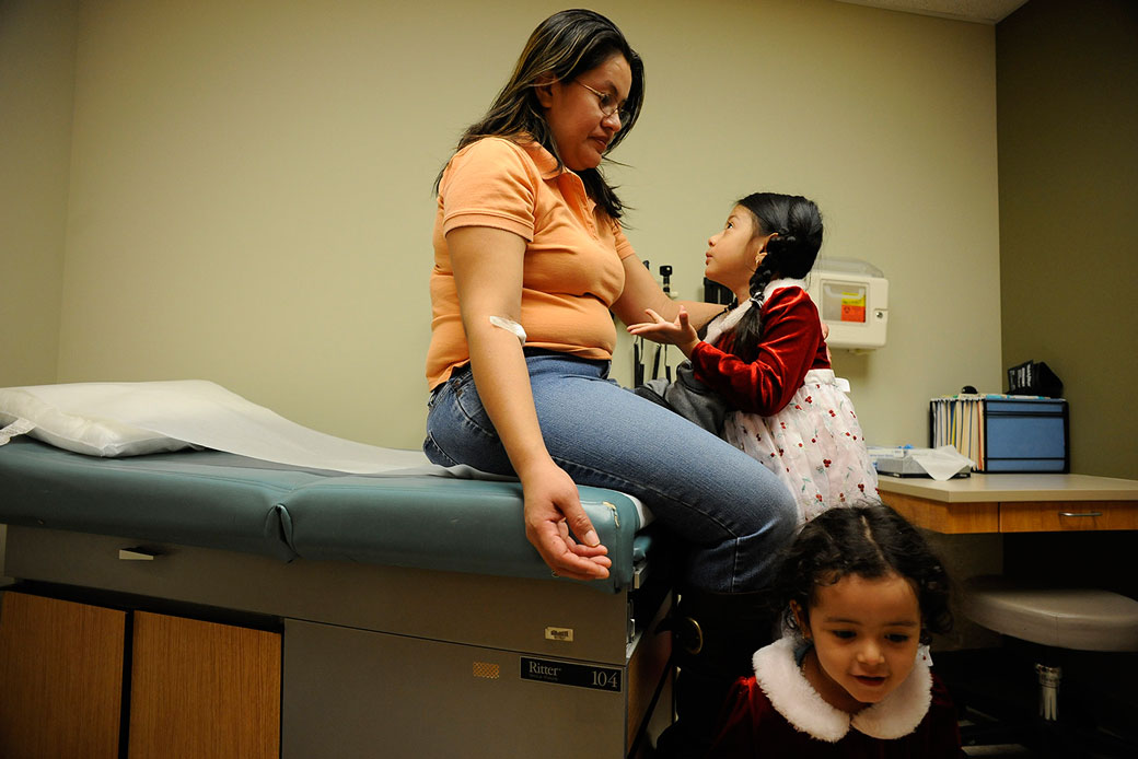  (A woman with her two young daughters sit in a doctor's office at a health services facility in Colorado.)