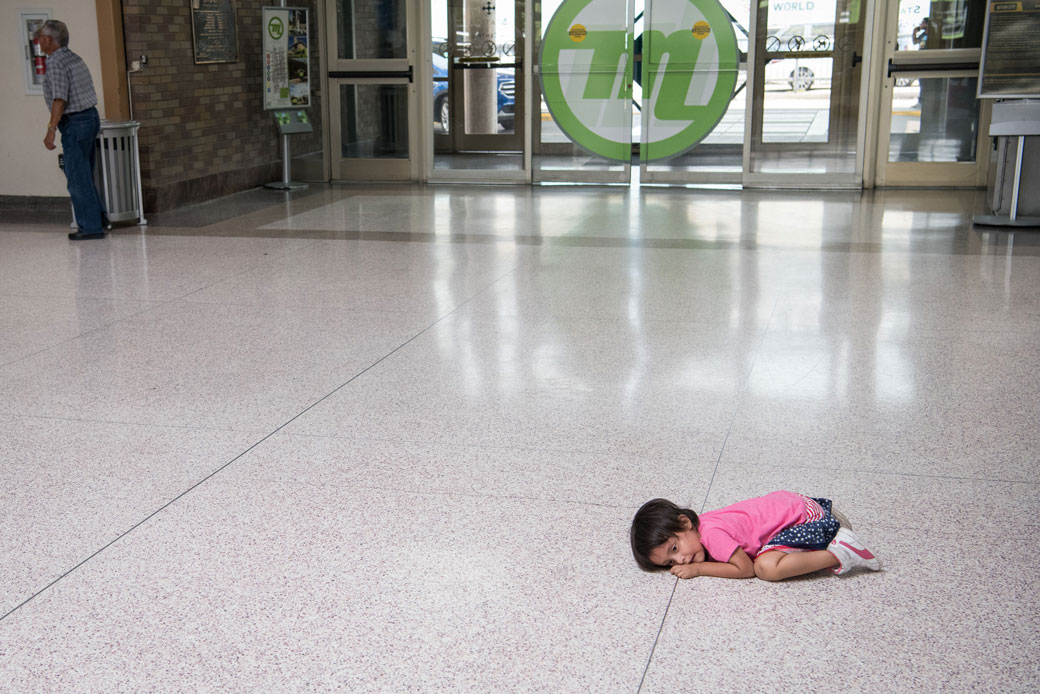A young migrant girl lies on the floor of a bus depot as her father, recently released from federal detention with other Central American asylum-seekers, obtains a ticket in McAllen, Texas, June 2019. (Getty/AFP/Loren Elliott)