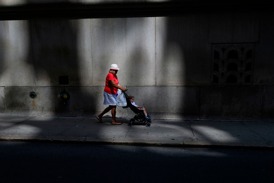  (A woman pushes a child in a stroller on a sidewalk.)