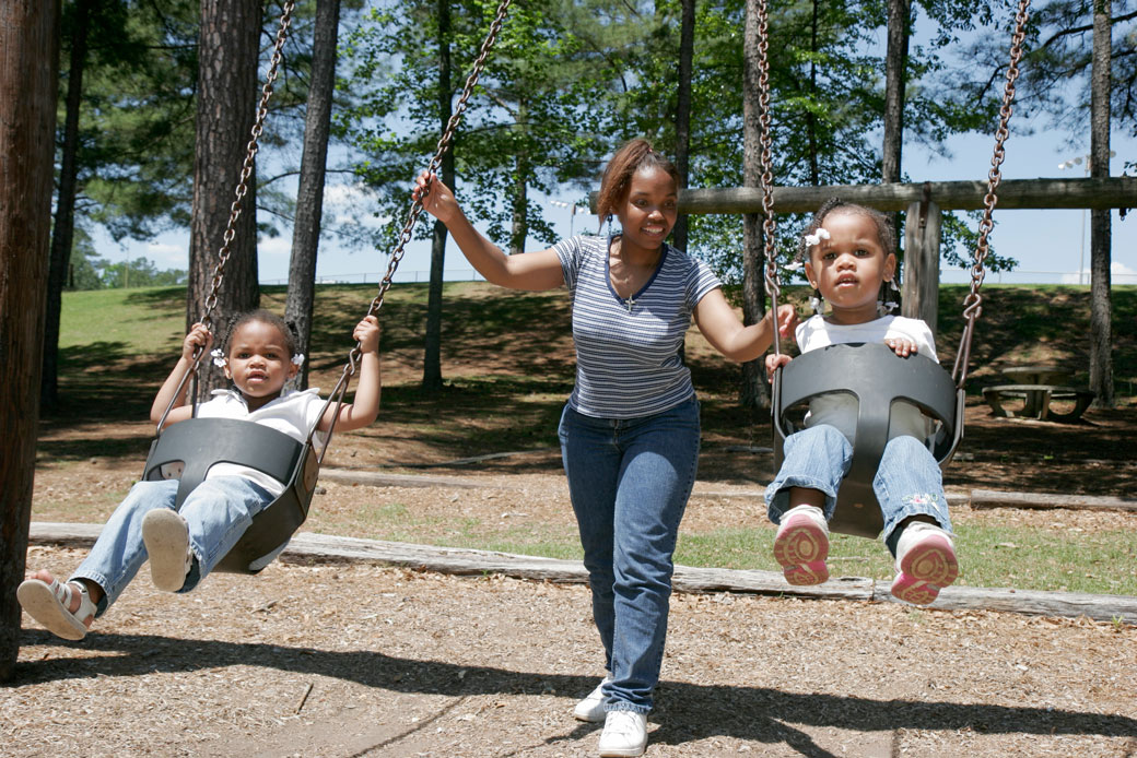  (A mother pushes her two young children on playground swings in Alabama.)