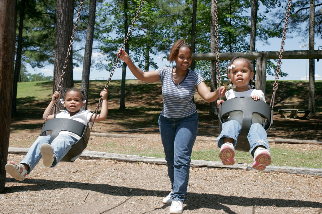 (A mother pushes her two young children on playground swings in Alabama.)