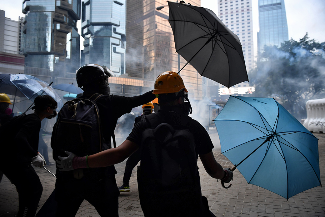  (A group of Hong Kong protesters wearing hard helmets and gas masks wards off tear gas with umbrellas.)