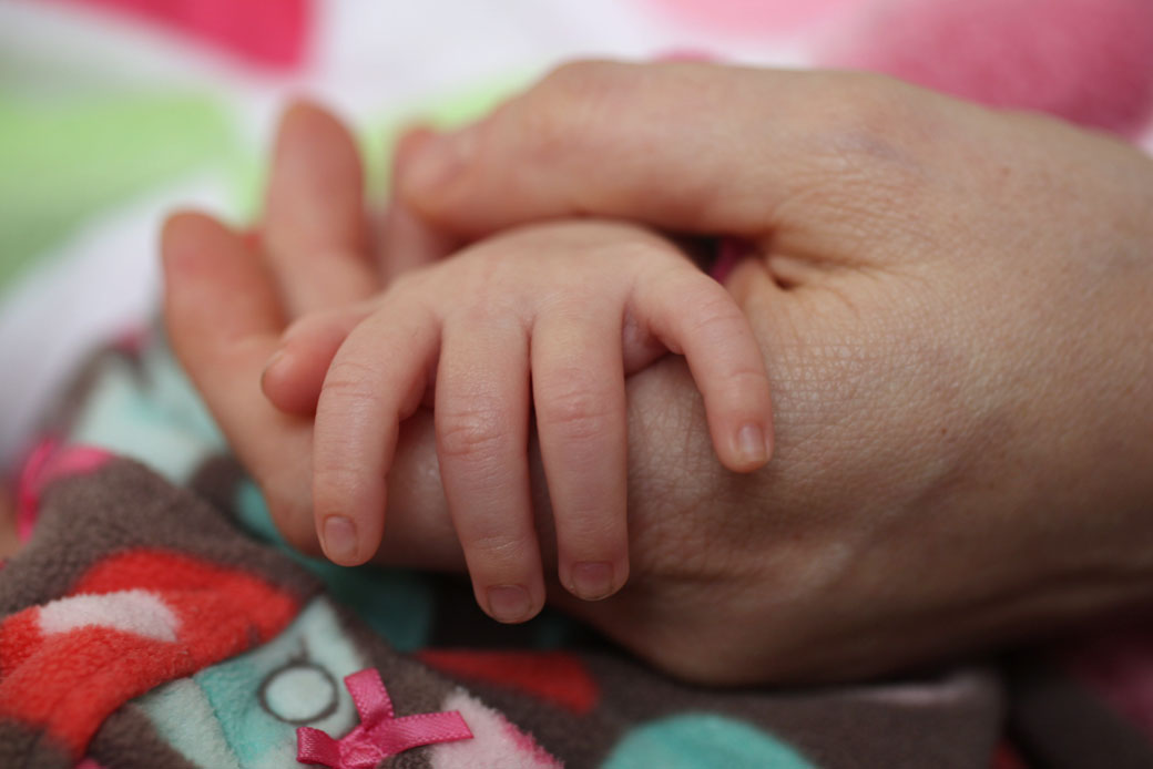 A mother holds her sleeping infant's hand. (Getty/Corbis News/Tim Clayton)