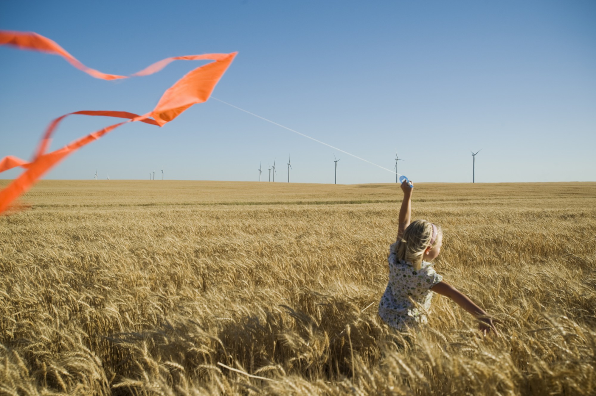 A girl runs with a kite on a wind farm. (Getty/Erik Isakson)