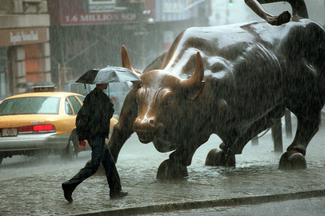  (A pedestrian walks past the Wall Street bull statue in New York City during heavy rain.)