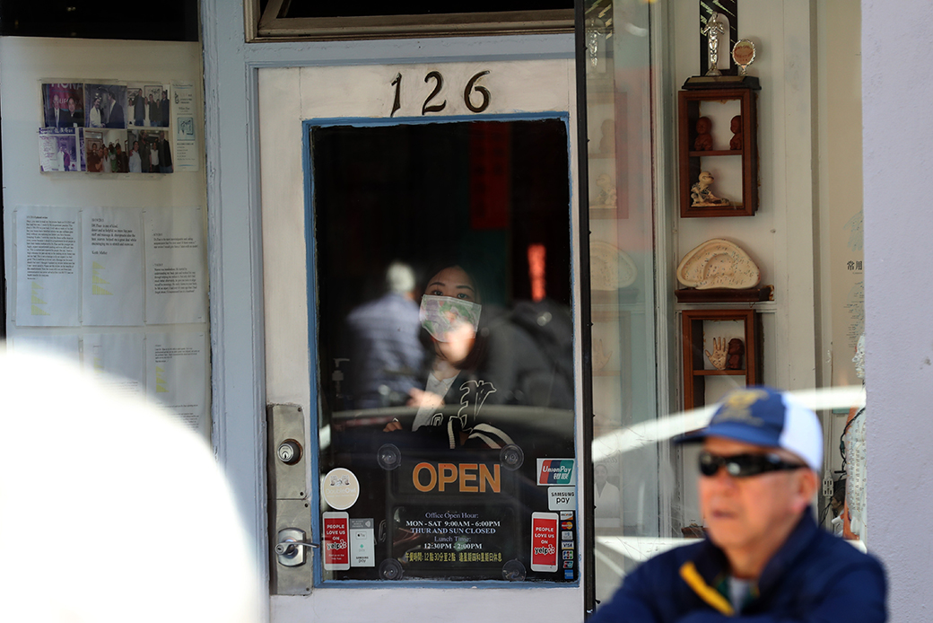 A woman wears a surgical mask as she looks out of a window, February 2020. (Getty/Justin Sullivan)