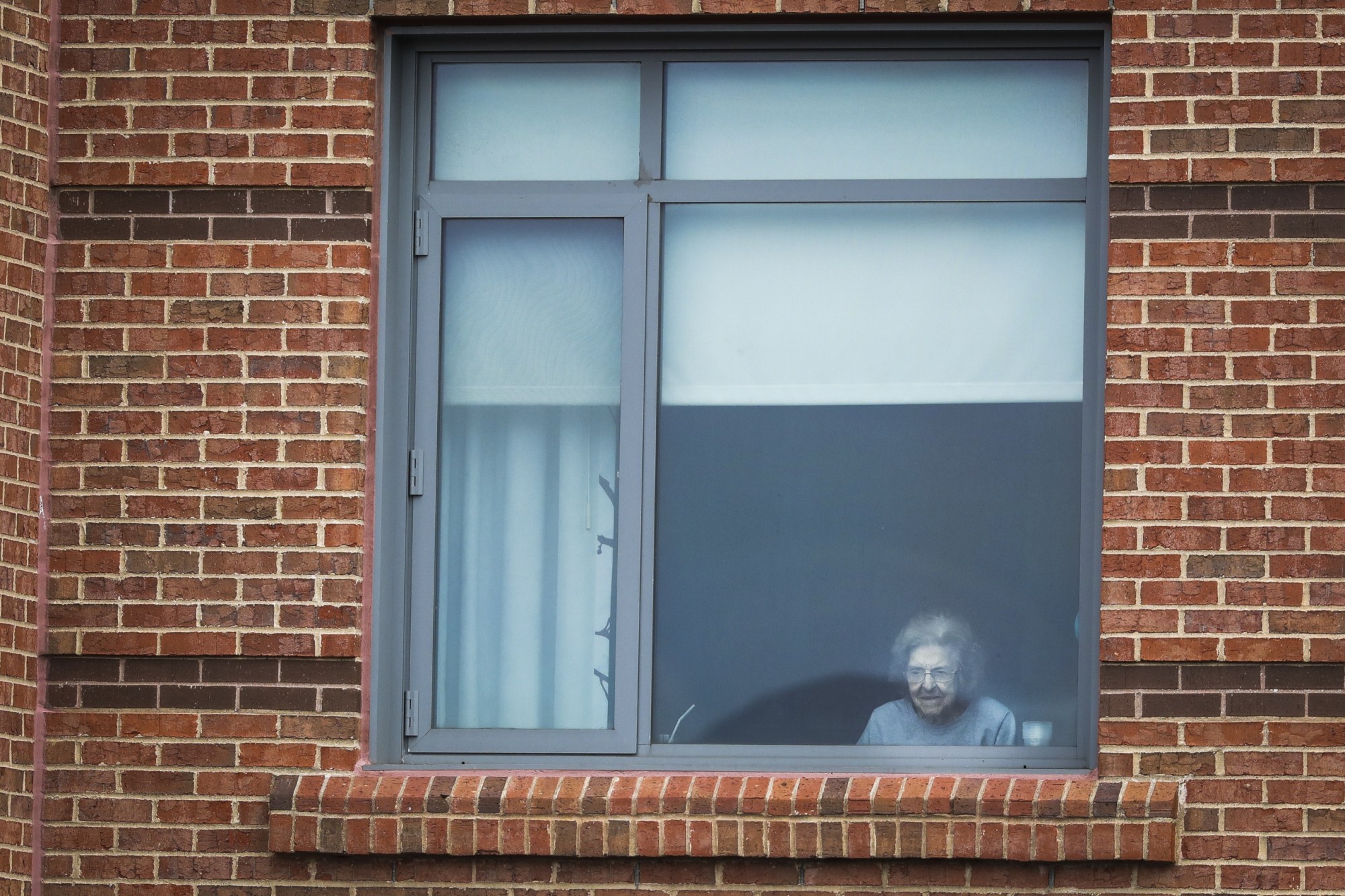 A resident at the Leonard Florence Center for Living watches from outside of her window as a three-piece-band performs from down below in Boston on March 20, 2020. (Getty/Erin Clark)