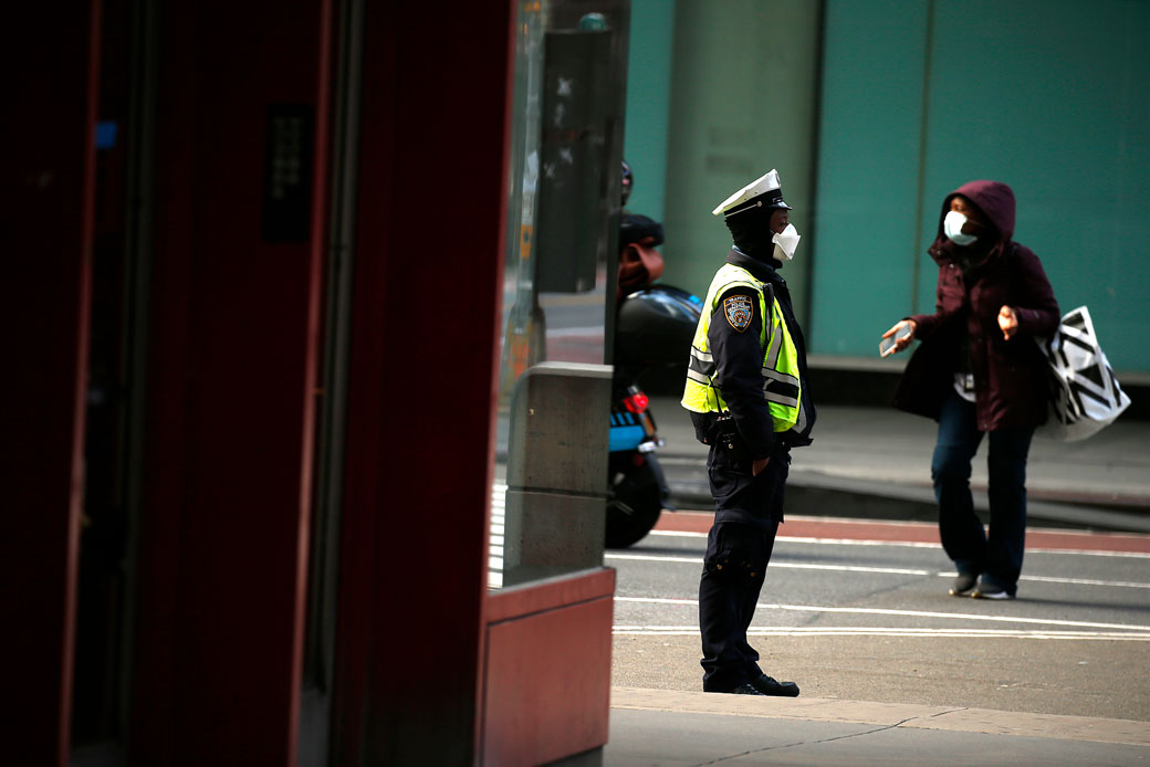 A NYPD police officer looks on as a woman crosses Seventh Avenue in New York City on April 12, 2020. (Getty/John Lamparski)