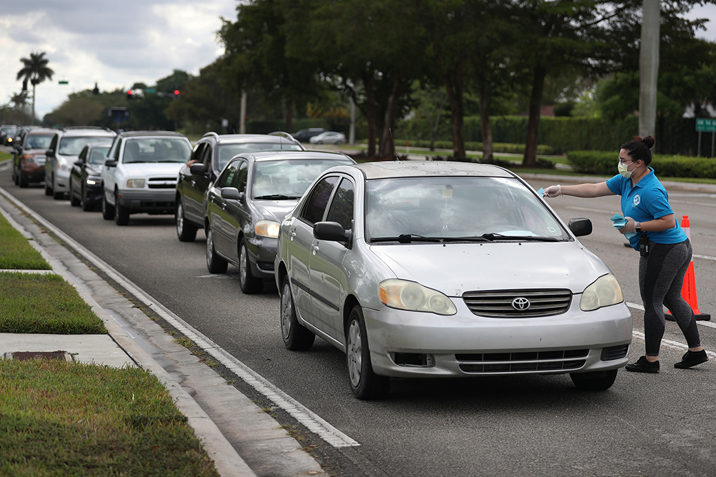 A woman gives vouchers for groceries, provided by the food bank Feeding South Florida, to people lined up in their vehicles on April 6, 2020, in Sunrise, Florida. (Getty/Joe Raedle)