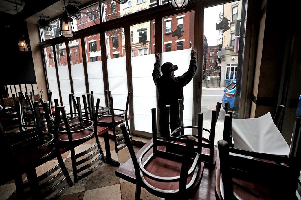 An employee at a Boston restaurant tapes paper in the windows following a statewide order to close all nonessential businesses in Massachusetts during the COVID-19 pandemic, March 2020. (Getty/The Boston Globe/David L. Ryan)