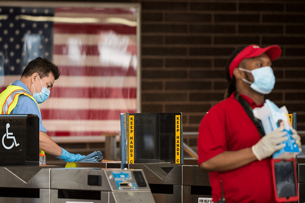 One transit employee wipes down the turnstiles while another passes out masks in the Ashmont Red Line station in Boston, June 2020. (Getty/Blake Nissen/The Boston Globe)