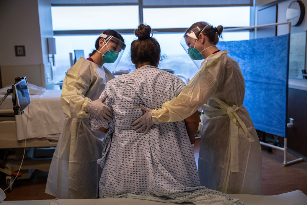  (Two hospital workers help a COVID-19 patient take her first steps after coming off a ventilator at a hospital in Stamford, Connecticut, on April 24, 2020.)