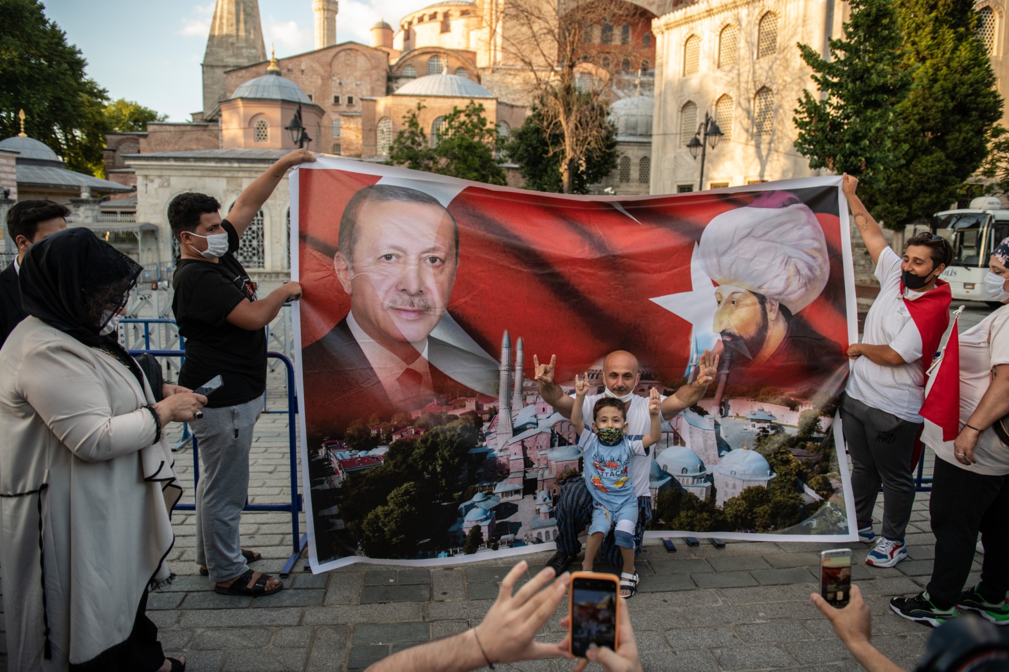 ISTANBUL, TURKEY - JULY 10: A man and a boy gesture in front of a placard depicting Turkish President Tayyip Erdogan and Ottoman Sultan Mehmet II, also known as Mehmet the Conqueror, outside Istanbul's famous Hagia Sophia on July 10, 2020 in Istanbul, Turkey. Turkey's top administrative court ruled to annul a 1934 decree that turned the historic Hagia Sophia into a museum. The controversial ruling opens the way for the structure to be converted back into a mosque after 85 years. President Recep Tayyip Erdoğan handed over the iconic structure’s control to the country’s Religious Affairs Directorate following a court ruling revoking its status as a museum. President Erdogan said that the government will open Istanbul’s Hagia Sophia for worship on July 24.  (Photo by Burak Kara/Getty Images)