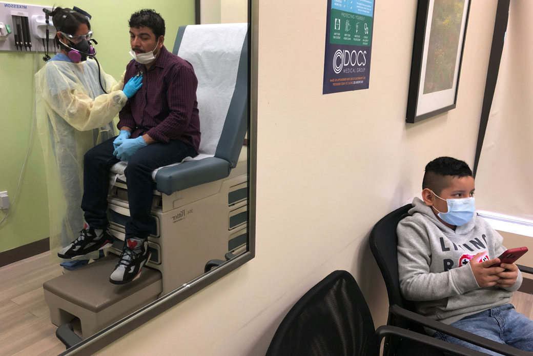 A boy waits as his father is checked by a physician's assistant before receiving a COVID-19 swab test at a clinic in Stamford, Connecticut, May 2020. (Getty/John Moore)