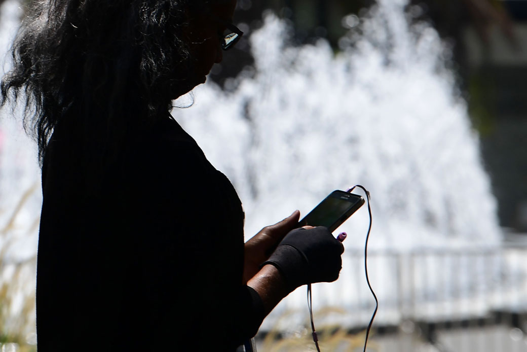A woman uses her cellphone while walking past a fountain in Los Angeles on August 13, 2019. (Getty/Frederic J. Brown/AFP)