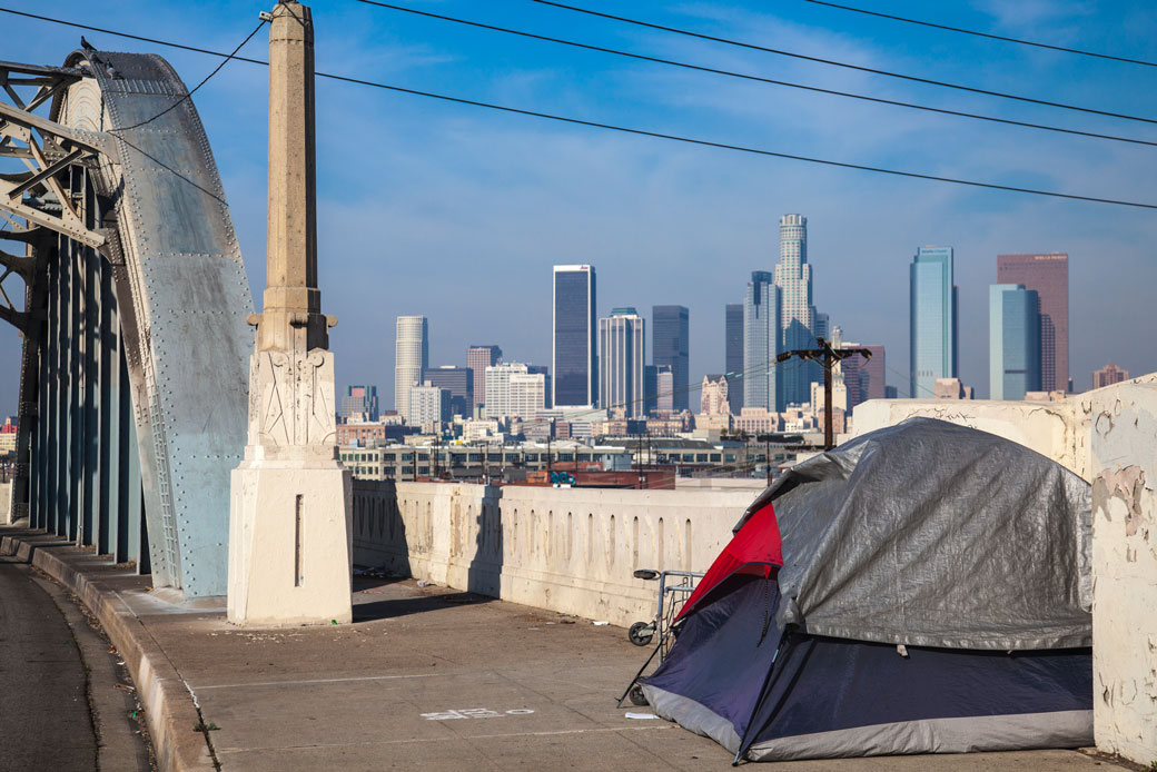 (The tent of a person experiencing homelessness sits on a bridge with the Los Angeles skyline in the background, January 2014.)