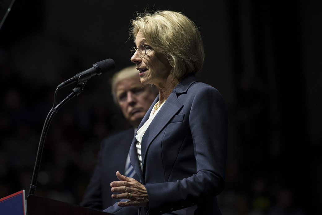 Then-President-elect Donald Trump looks on as Betsy DeVos, now his secretary of education, speaks at an arena, December 2016, in Grand Rapids, Michigan. (Getty/Drew Angerer)