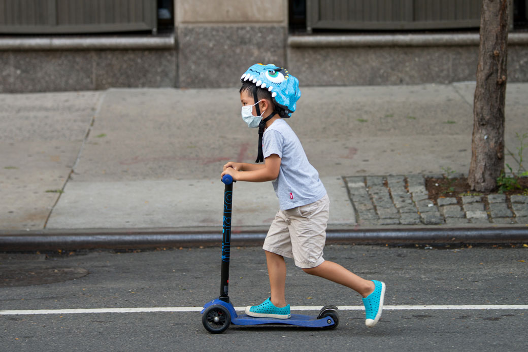 A child wearing a mask rides a scooter down the street in New York City, July 2020. (Getty/Alexi Rosenfeld)