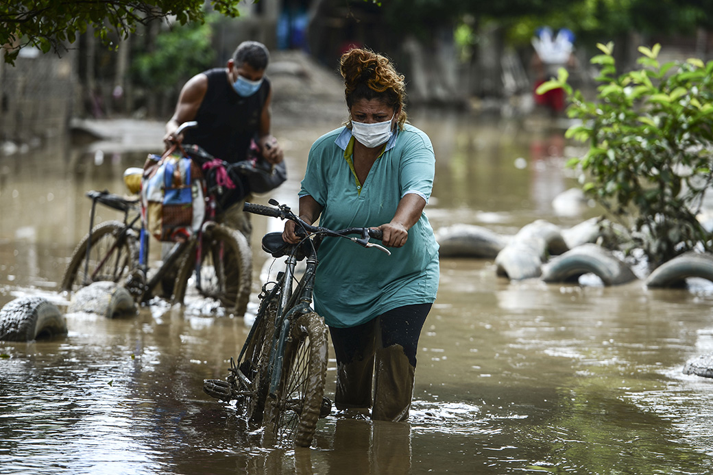 A Honduran family who fled from the flooded La Guadalupe municipality with just two bikes and some clothes advances through the muddy water in the also-flooded municipality of La Lima near San Pedro Sula, November 20, 2020, after the passage of Hurricane Iota. (Getty/Orlando Sierra/AFP)