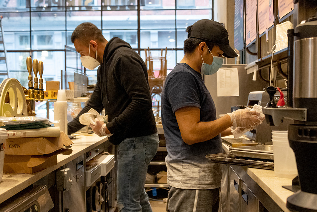 Two employees wearing masks and gloves clean inside a restaurant as it prepares to reopen for takeaway and delivery orders after being closed for more than a month amid the coronavirus pandemic, May 2020, in New York City. (Getty/Alexi Rosenfeld)