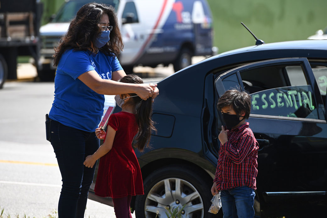 A mother puts a mask on her children as day laborers and their supporters participate in a 