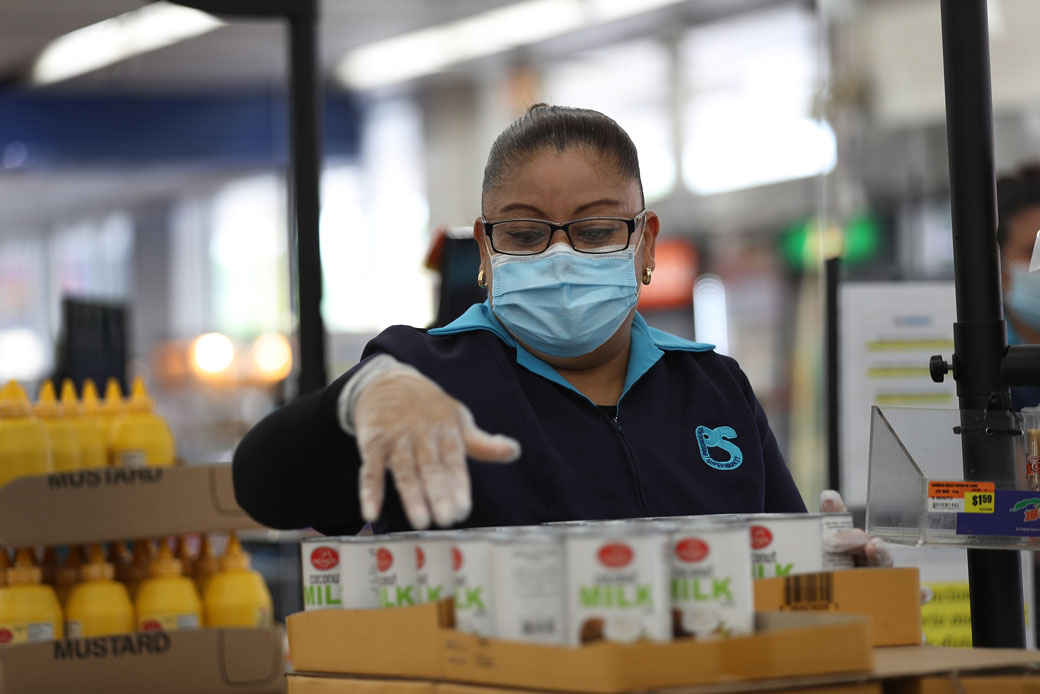 A woman wears a mask and gloves as she works as a cashier at a supermarket in Miami, April 2020. (Getty/Joe Raedle)