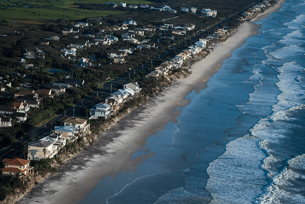  (Bird's-eye view of houses along an eroded beach/shoreline close to the water's edge.)