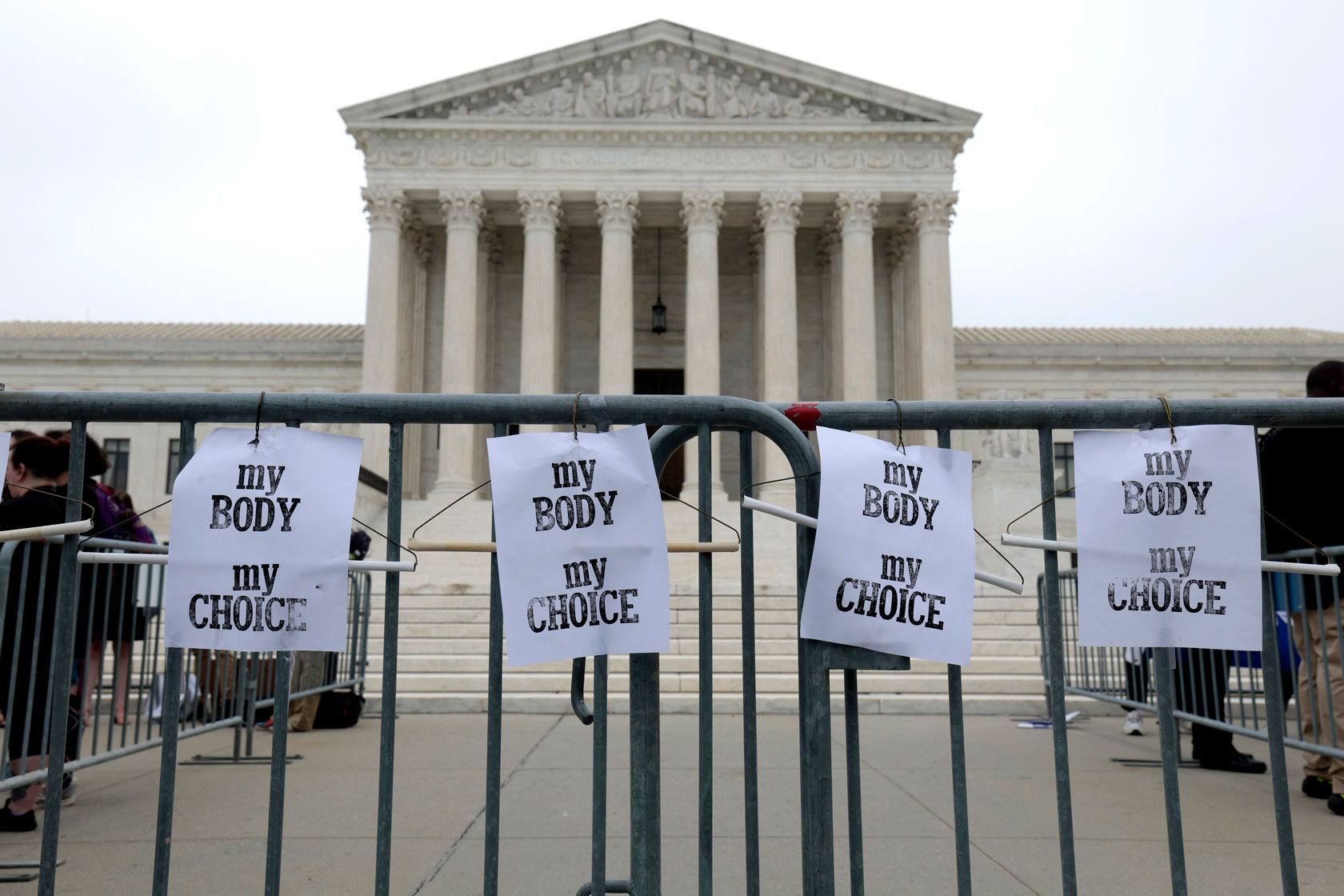 Photo shows four signs hanging on a fence in front of the Supreme Court building. The signs read 