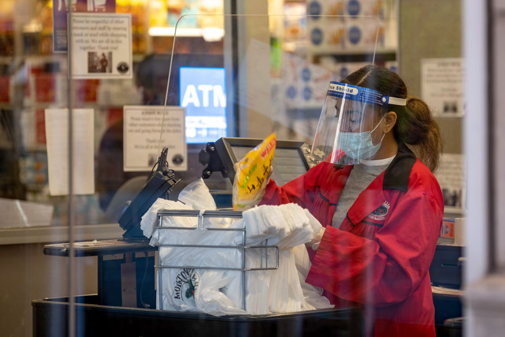 A New York City supermarket employee wears a mask, face shield, and gloves as she bags groceries on April 28, 2020. (Getty/Alexi Rosenfeld)