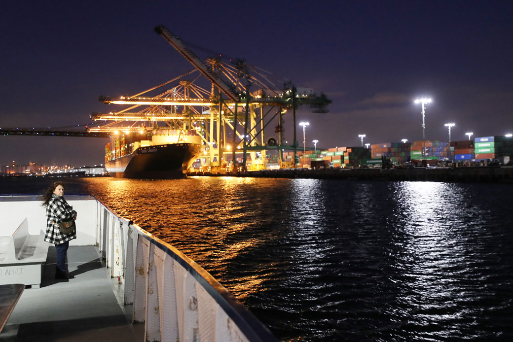  (A woman rides on a tour boat as a container ship is offloaded at the Port of Los Angeles in Terminal Island, California, March 2020.)