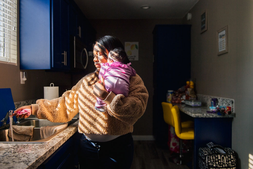 A mother holds her young child as she runs the faucet before a meeting with family over Zoom on November 26, 2020, in Los Angeles. (Getty/Brandon Bell)
