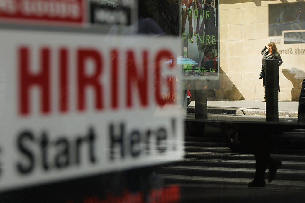  (Close-up reflection of a white sign with red and black text in a window reading 