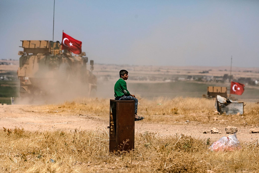  (A boy watches a Turkish military convoy drive past a Syrian village on the outskirts of Tal Abyad along the border with Turkey, September 2019.)